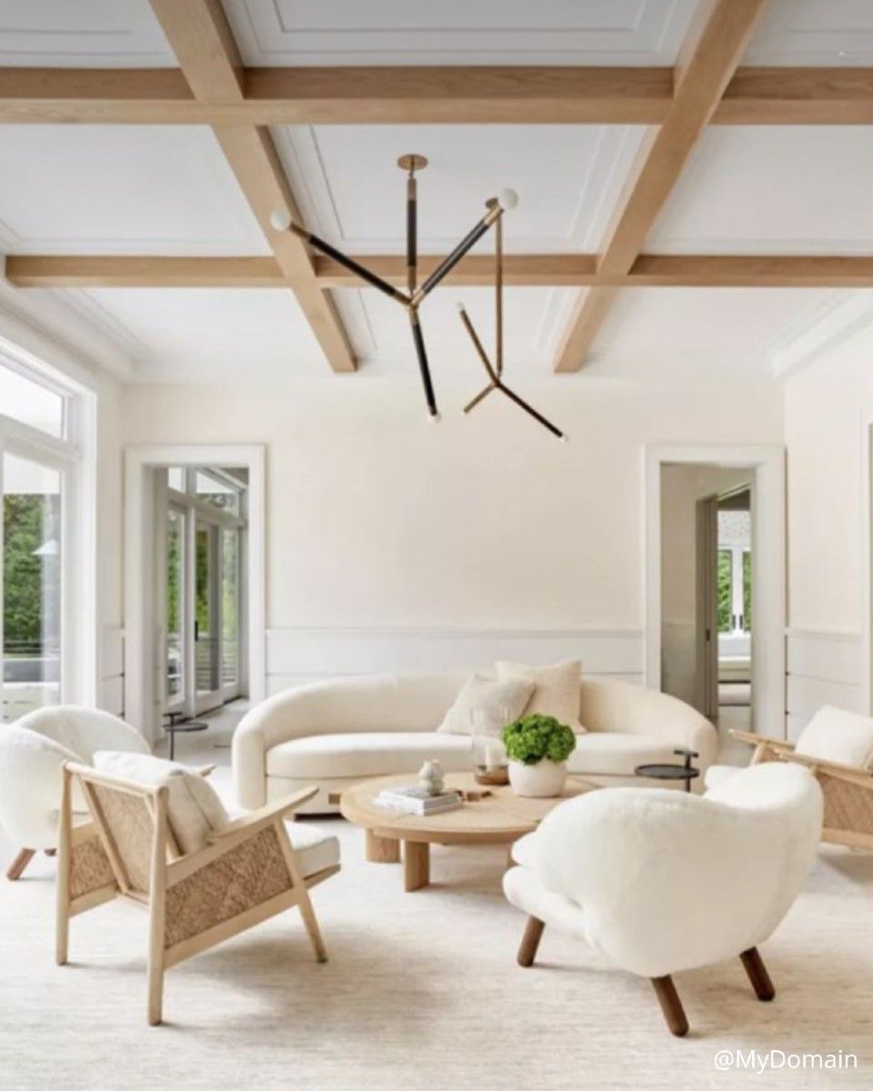 Salon aux murs couleur crème, avec canapé incurvé et touches de bois. Un lustre moderne est suspendu au plafond.