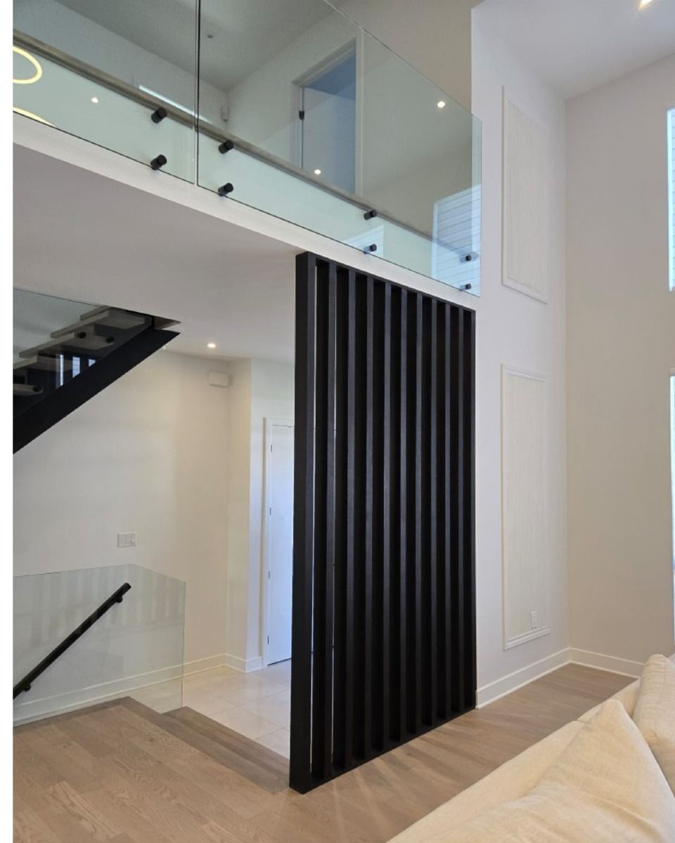 Cloison à lattes noires dans l'entrée d'une maison moderne, séparant le hall d'entrée de la pièce à vivre.