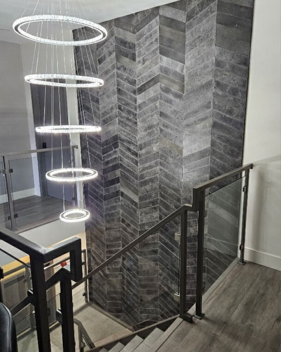 Escalier avec un mur d'accent à motif à chevrons gris foncé, une rampe en verre et un lustre circulaire.