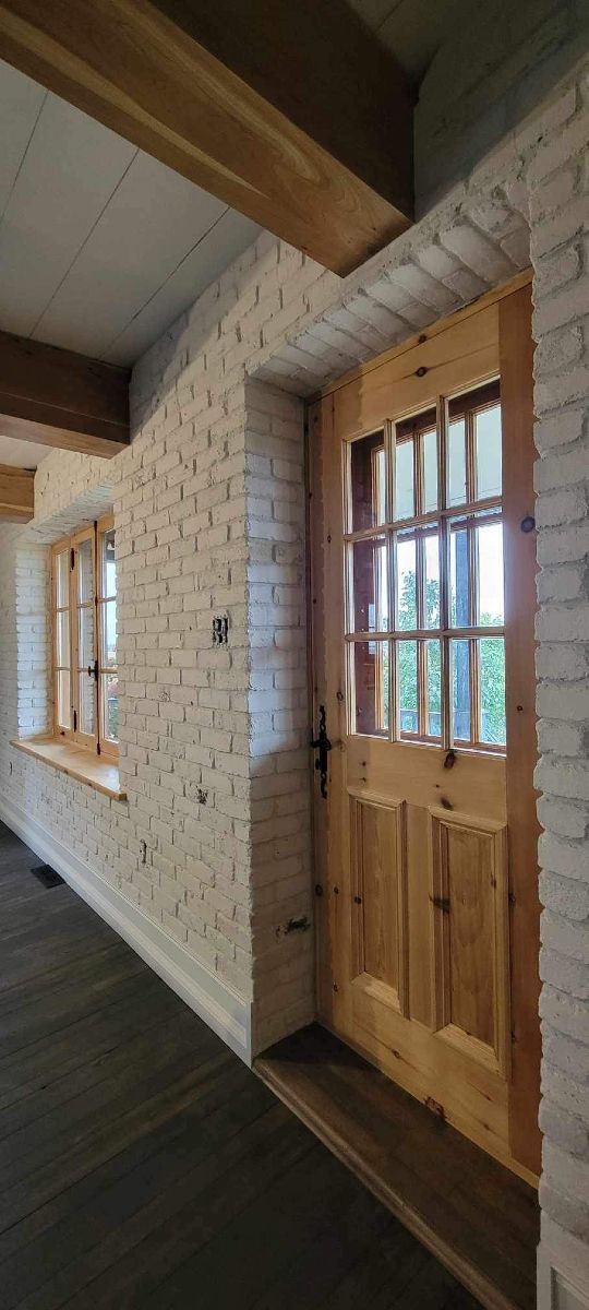 Vue intérieure d'une pièce rustique avec une porte en bois, des murs en briques et une fenêtre, montrant un espace chaleureux et accueillant.
