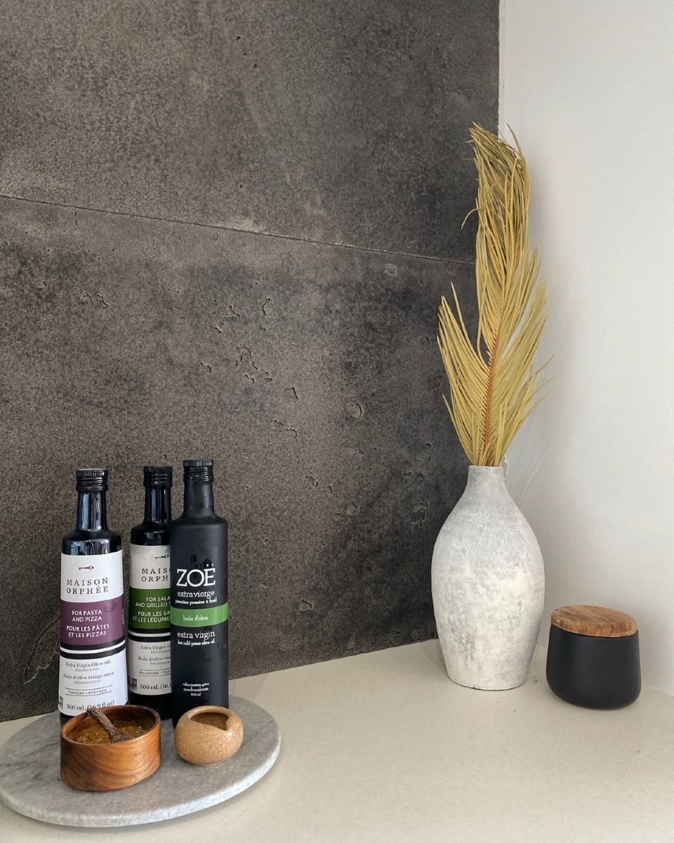 Bouteilles d'huile d'olive et d'épices sur un plateau en marbre avec un vase et des plantes séchées contre un mur gris et blanc.