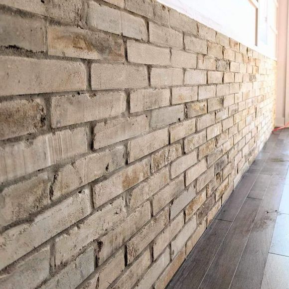 Mur de briques de couleur crème avec une légère perspective en angle, à côté d'un plancher en bois.