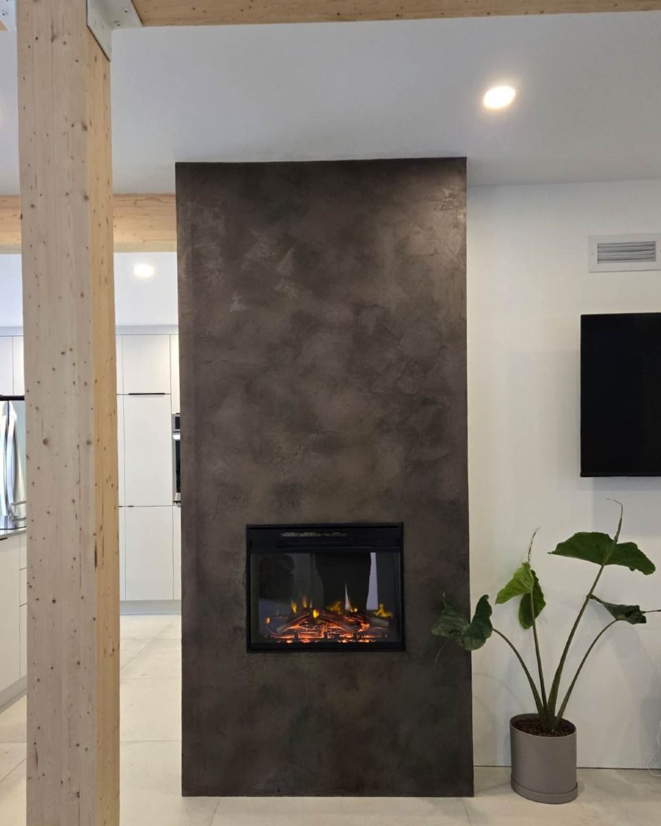 Cheminée moderne encastrée dans un mur texturé brun foncé, avec une plante et une colonne en bois clair à proximité.