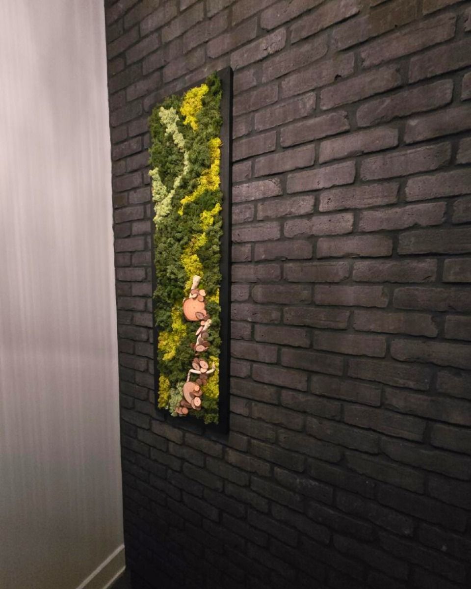 Art de mousse vivante dans un cadre noir sur un mur de briques sombres.