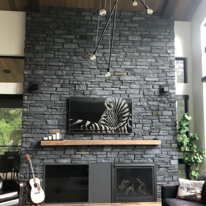 Mur d'accent en pierre avec cheminée, télévision et œuvre d'art zébrée. Manteau de cheminée en bois, armoires noires et guitare.