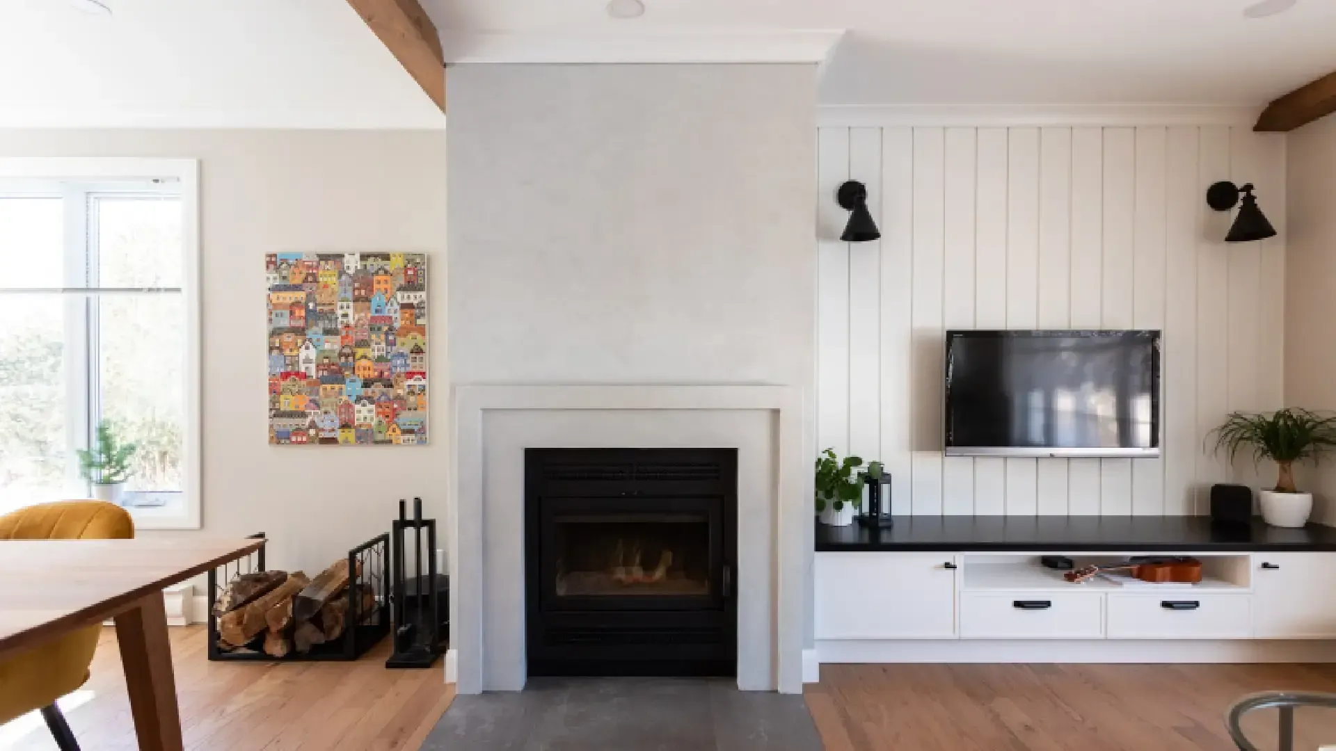 Séjour avec cheminée, TV, mur en planches à clin blanches et poutres en bois.