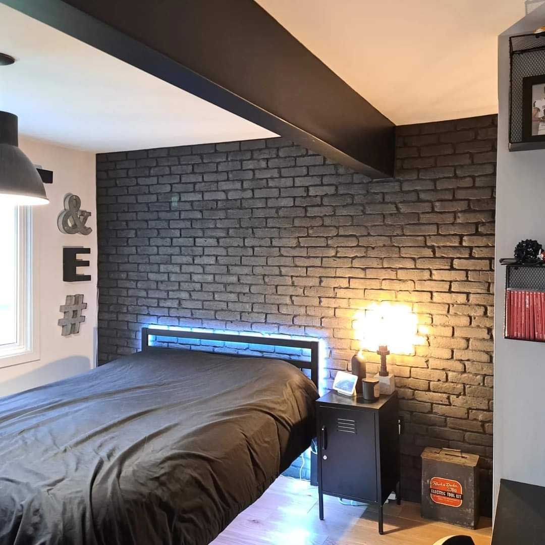 Chambre avec mur d'accent en briques grises, lit, lampes suspendues et art neutre.