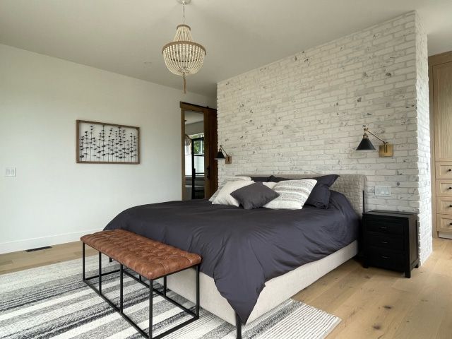 Chambre avec mur de briques blanchies à la chaux, lit avec literie foncée, banc, tapis, lustre.