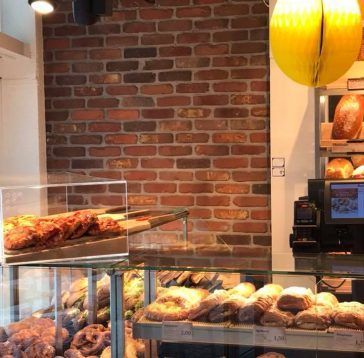 Intérieur de boulangerie : mur de briques, présentoir à pain, petits pains, viennoiseries, comptoir.