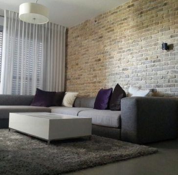 Salon avec canapé sectionnel gris, mur de briques, tapis et table basse blanche.