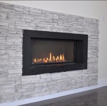 Cheminée avec cadre noir encastrée dans un mur en pierre gris clair, flammes visibles à l'intérieur.