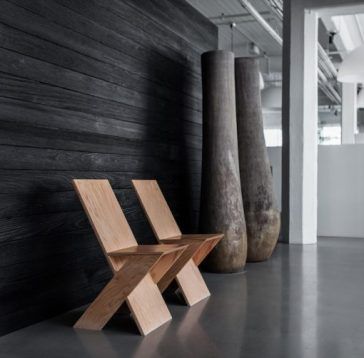 Deux chaises en bois contre un mur sombre avec trois grands vases ; sol gris et mur blanc en arrière-plan.