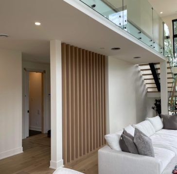 Salon moderne avec canapé sectionnel blanc, mur en lattes de bois et escalier ouvert.
