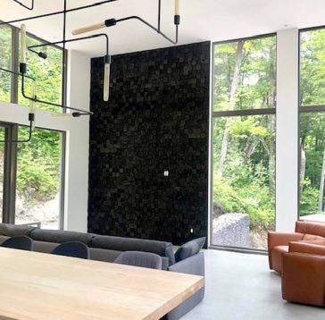 Salon moderne avec mur d'accent sombre et grandes fenêtres donnant sur une forêt.