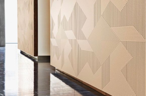 Panneaux muraux en bois à motifs géométriques dans un couloir intérieur avec sol réfléchissant.