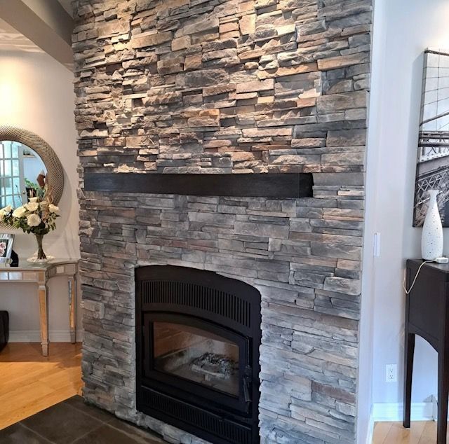 Cheminée en pierre avec insert et manteau noirs. Aménagement intérieur avec parquet et décoration en bois.