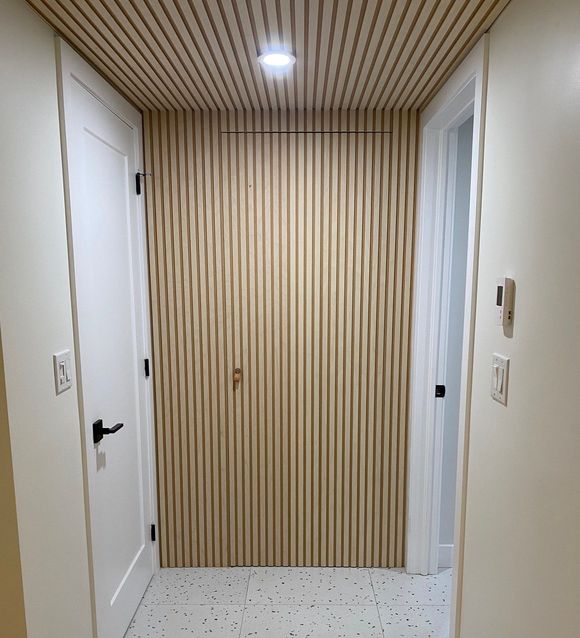 Couloir avec murs et plafond en lattes de bois, deux portes blanches, sol de couleur claire et luminaires.