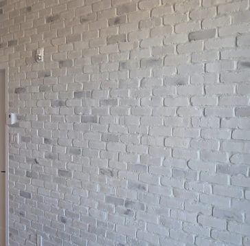 Mur de briques peintes en blanc avec un encadrement de porte à gauche. Installations électriques visibles.