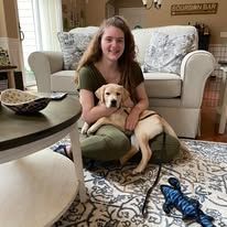Woman sitting on the floor holding a yellow puppy in a living room with a couch and rug