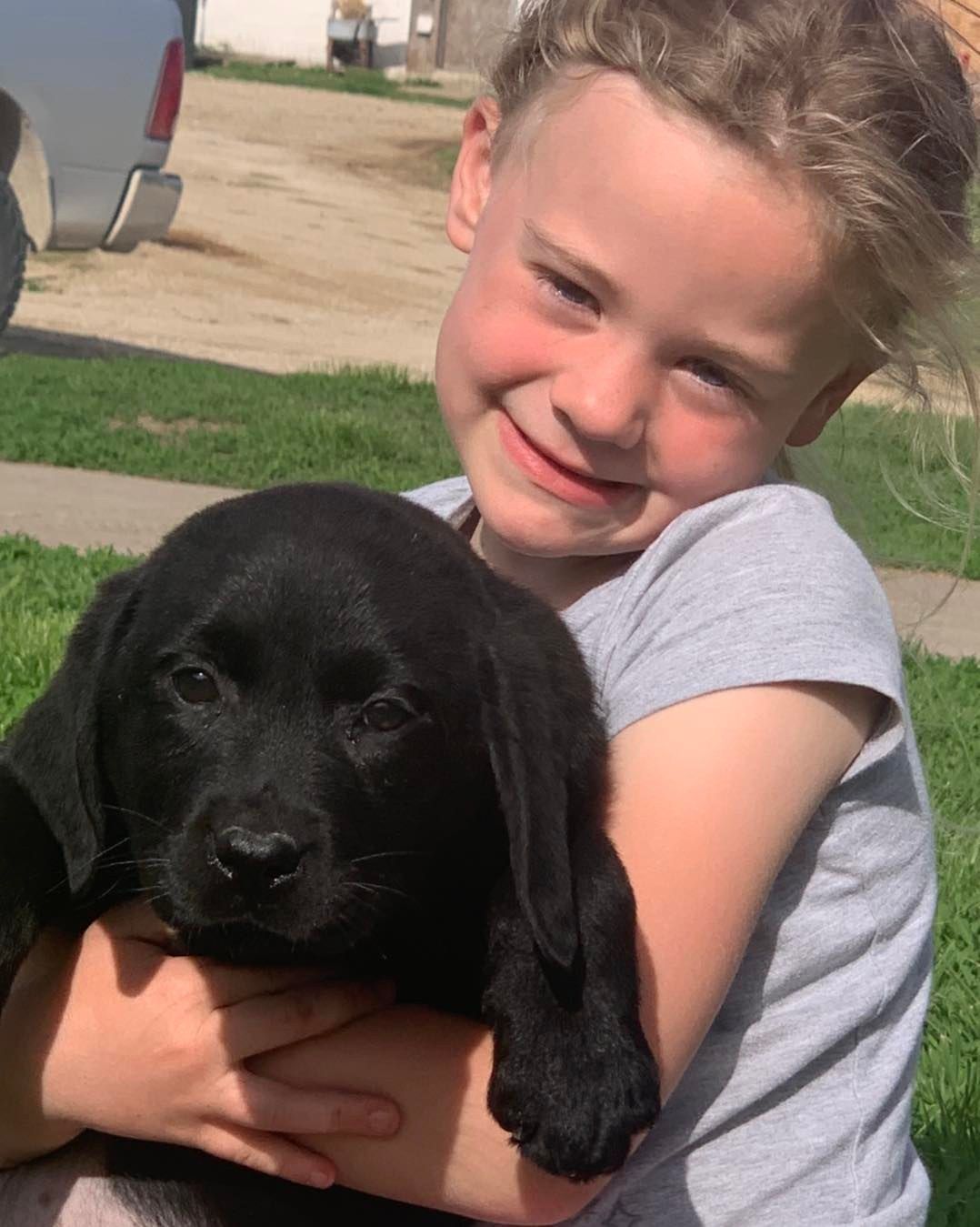 Smiling child holding a black puppy outdoors in bright sunlight
