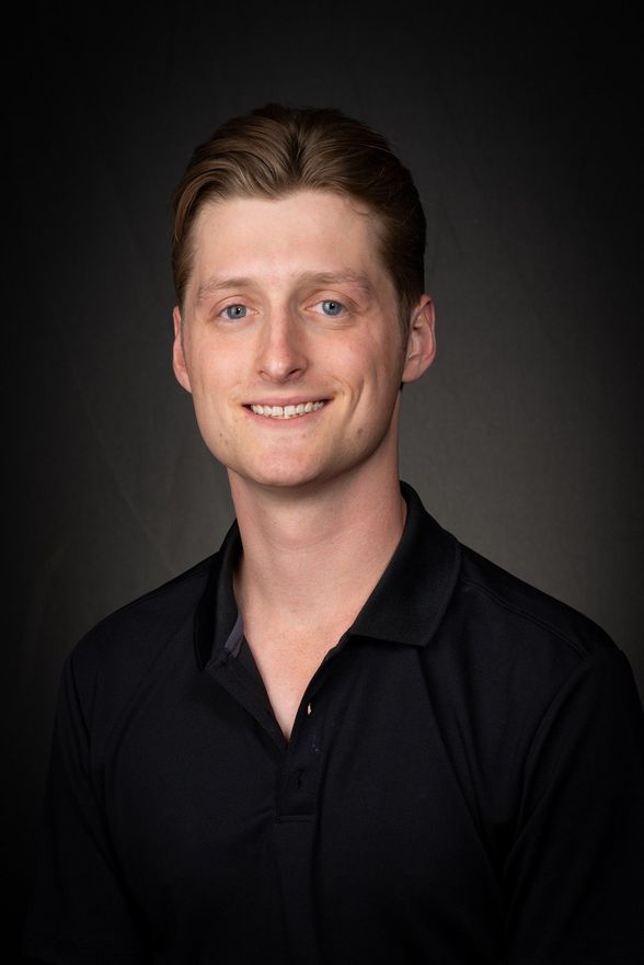 Studio portrait of a smiling Ryan DePascalis in a black shirt against a dark background
