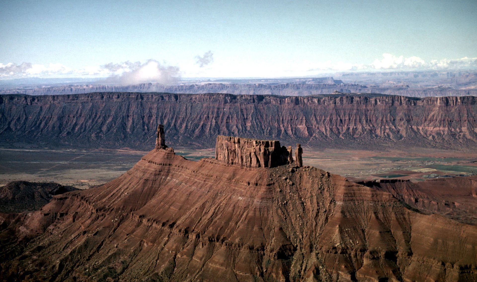Mesa butte in a vast desert landscape beneath cloudy mountains