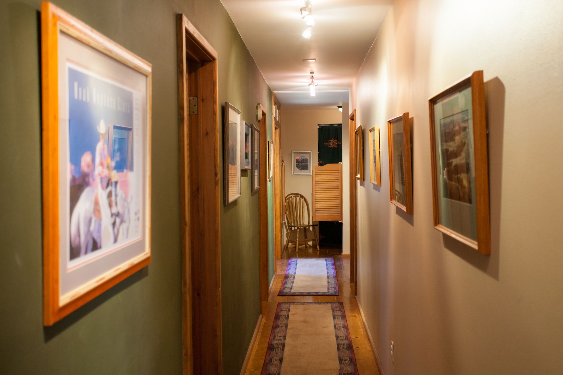 Narrow hallway with framed pictures on both walls and a runner rug on the floor