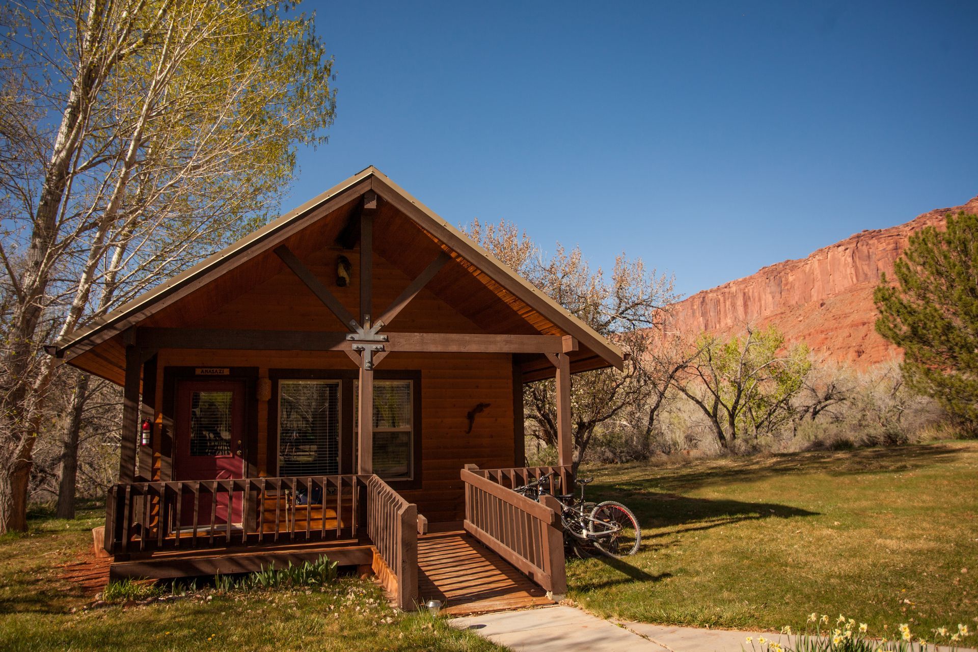 Rustic log cabin with porch and ramp in a sunny autumn landscape with red cliffs and trees