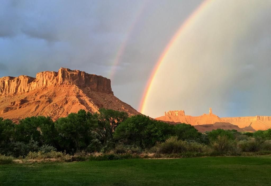 Rainbow over red sandstone cliffs and green field at sunset