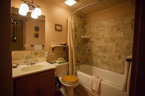Warm-lit bathroom with sink, toilet, and bathtub with stone-patterned shower wall