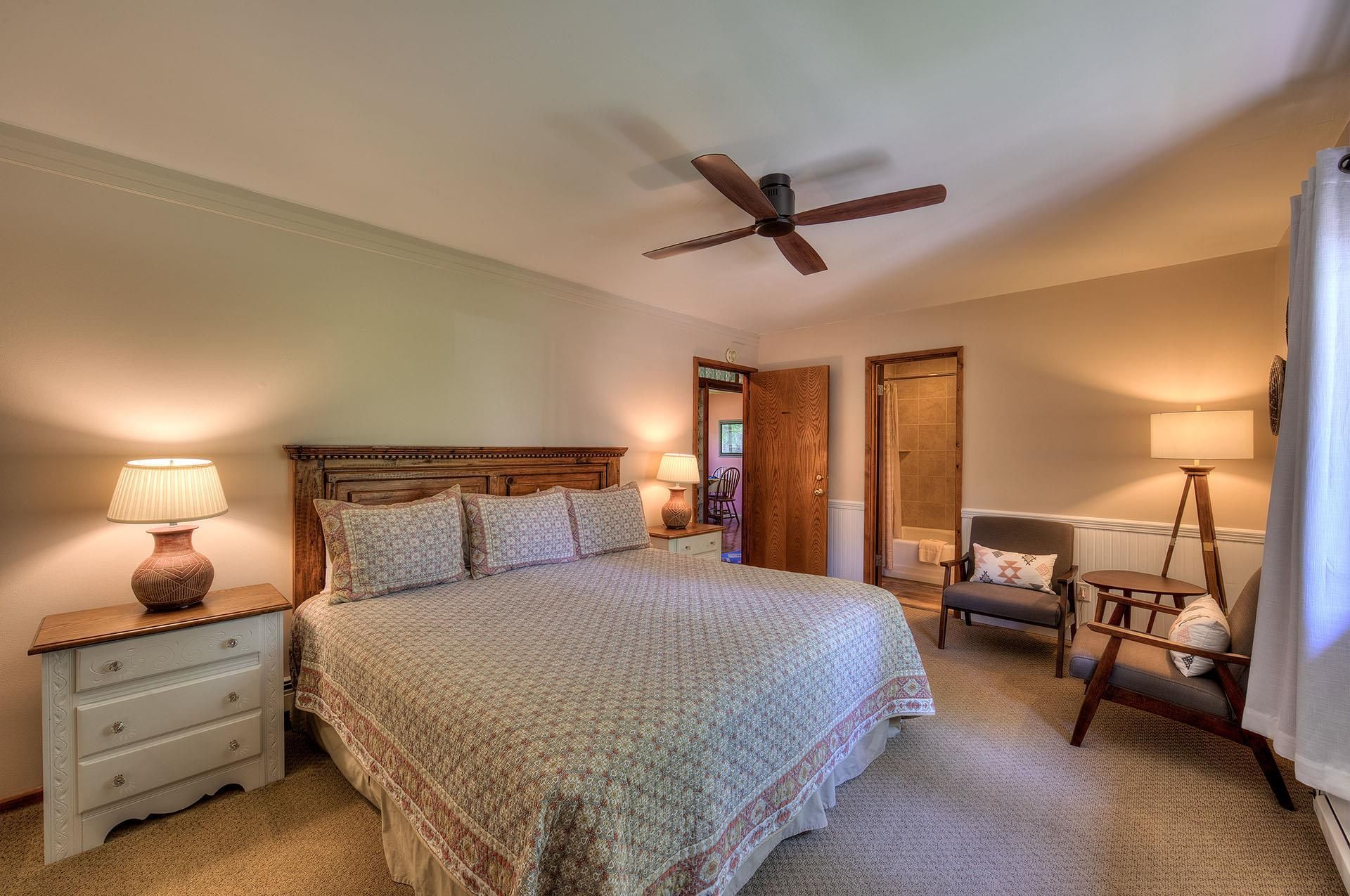 Cozy bedroom with king bed, nightstands, lamps, ceiling fan, chair, and open closet doors