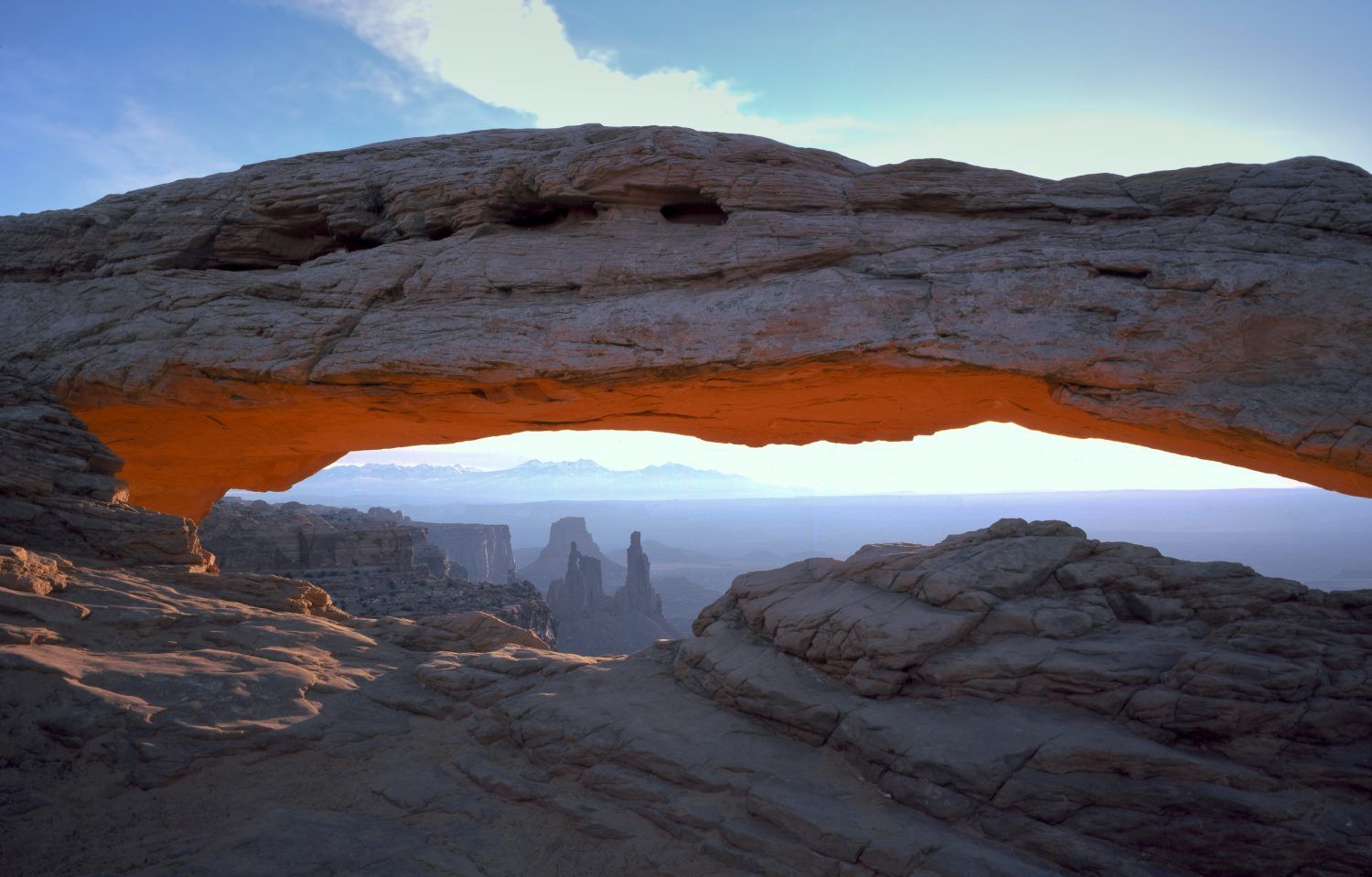 Natural rock arch framing a sunrise over a desert canyon landscape