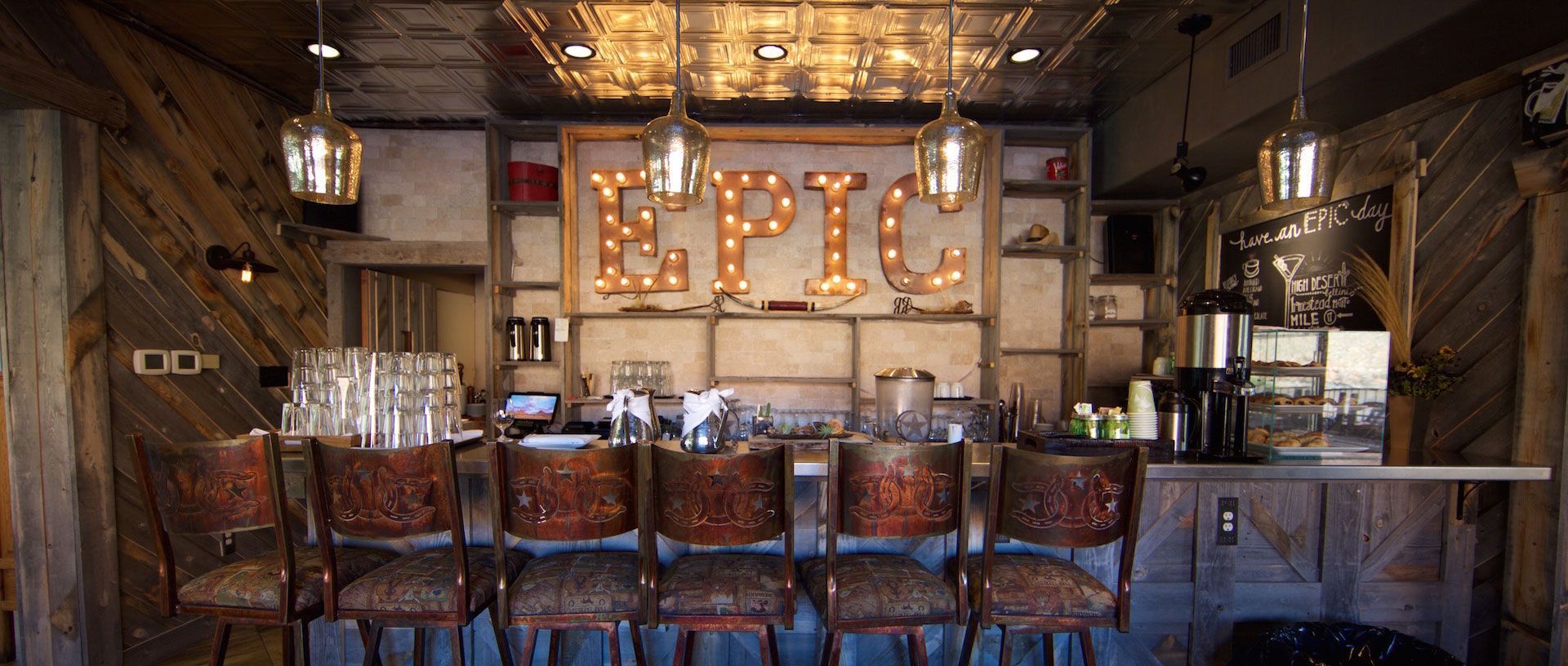 Rustic bar interior with glowing “EPIC” marquee sign and rows of wooden chairs and tables