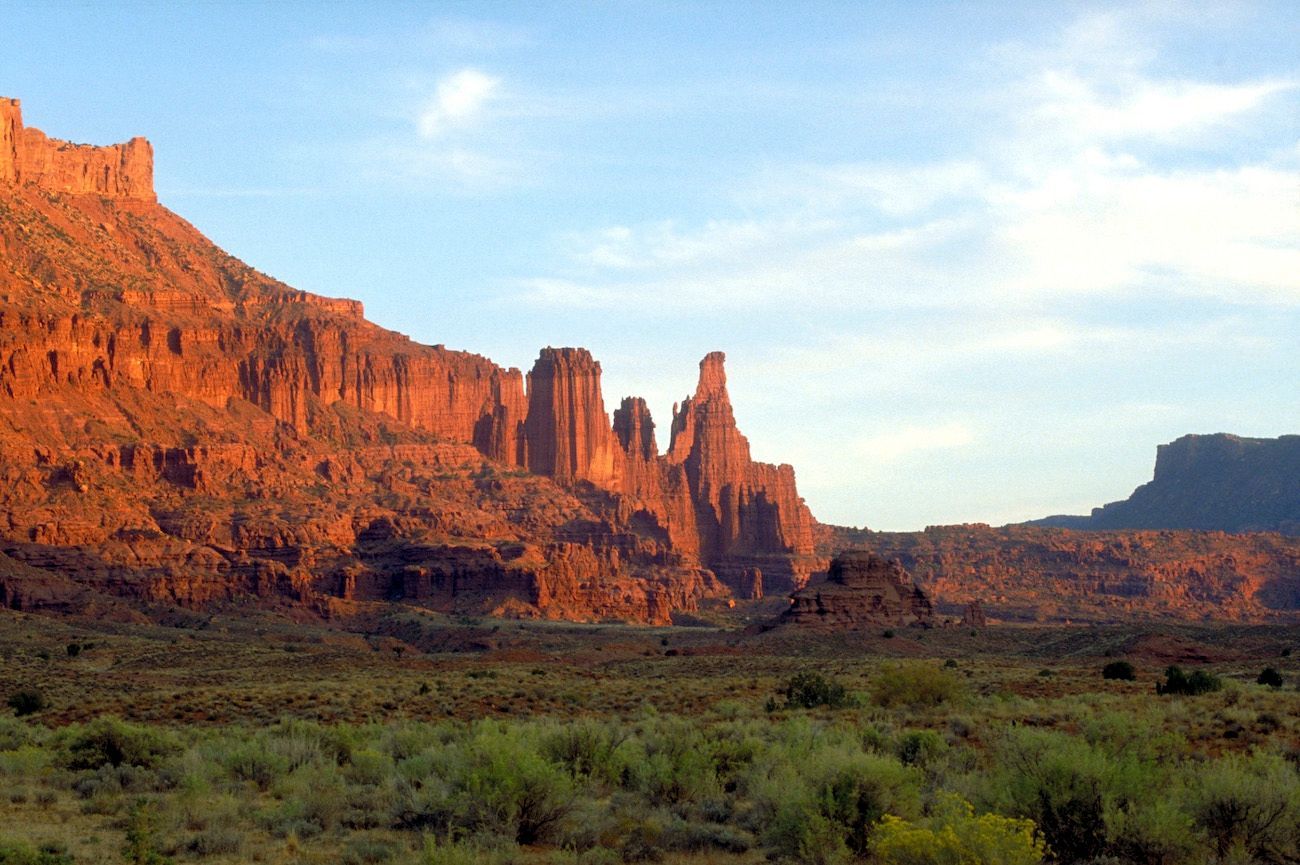 Sunlit red rock canyon cliffs under a blue sky with sparse desert vegetation