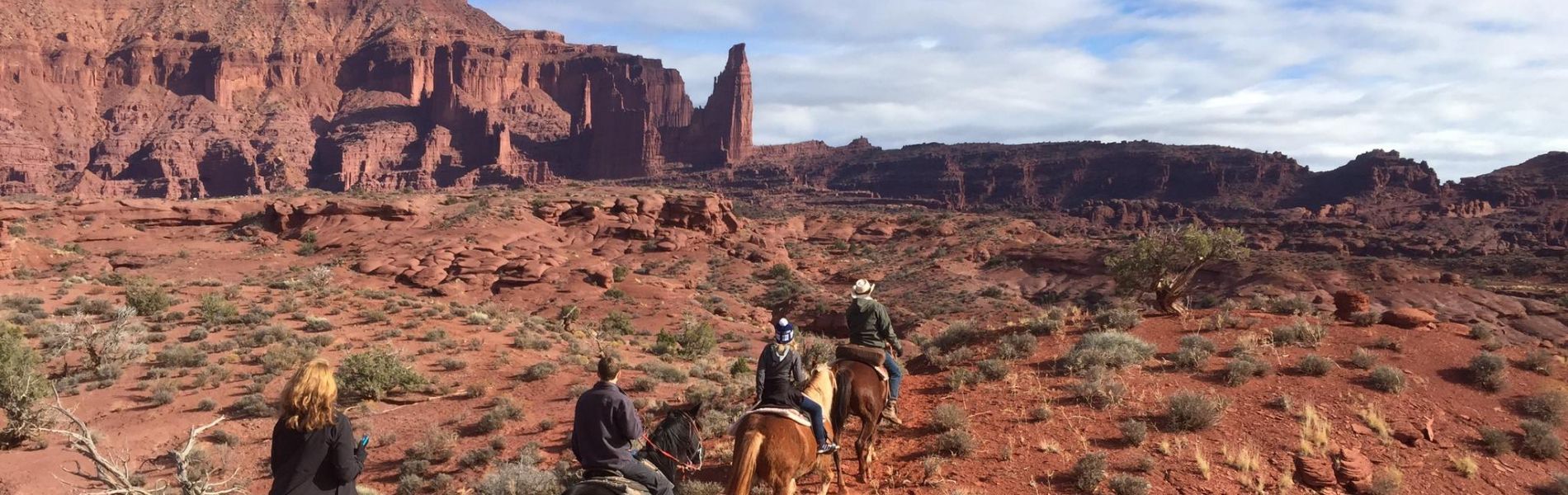 Hikers on horseback traversing a rocky red desert canyon under towering cliffs
