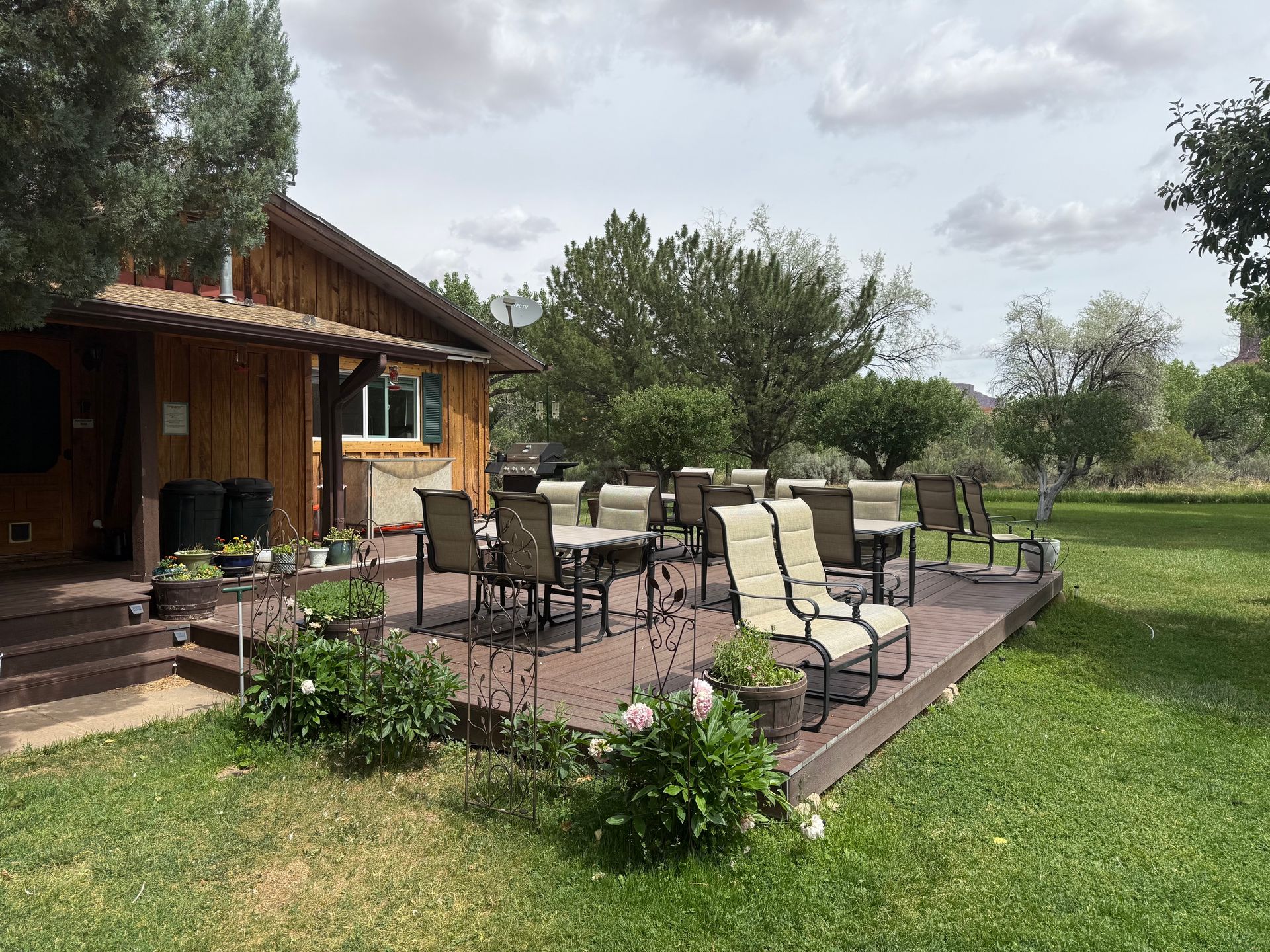 Patio with outdoor chairs and tables beside a wooden house, surrounded by grass and trees.