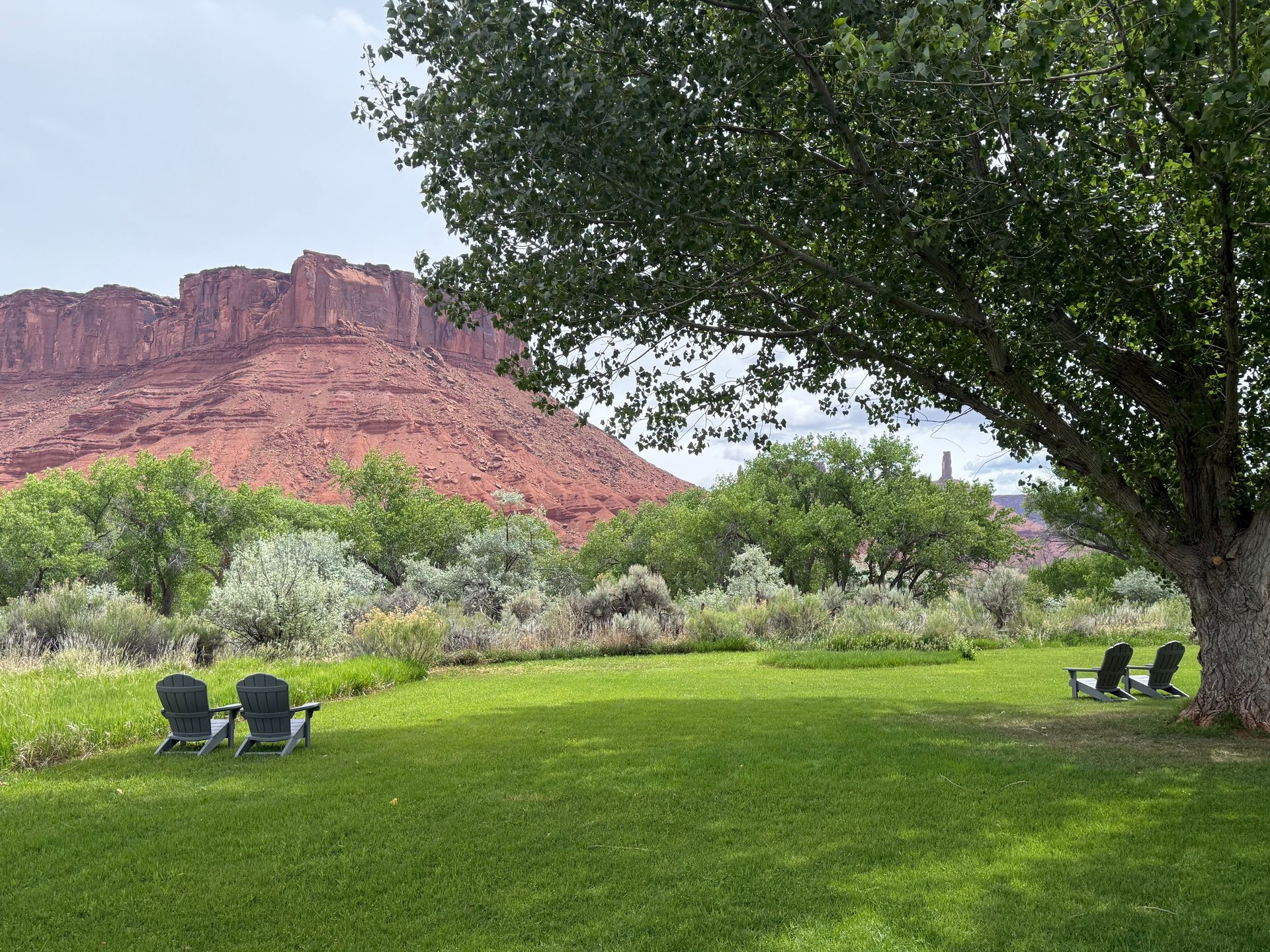 Grassy park with lawn chairs, trees, and red sandstone cliffs under a cloudy sky