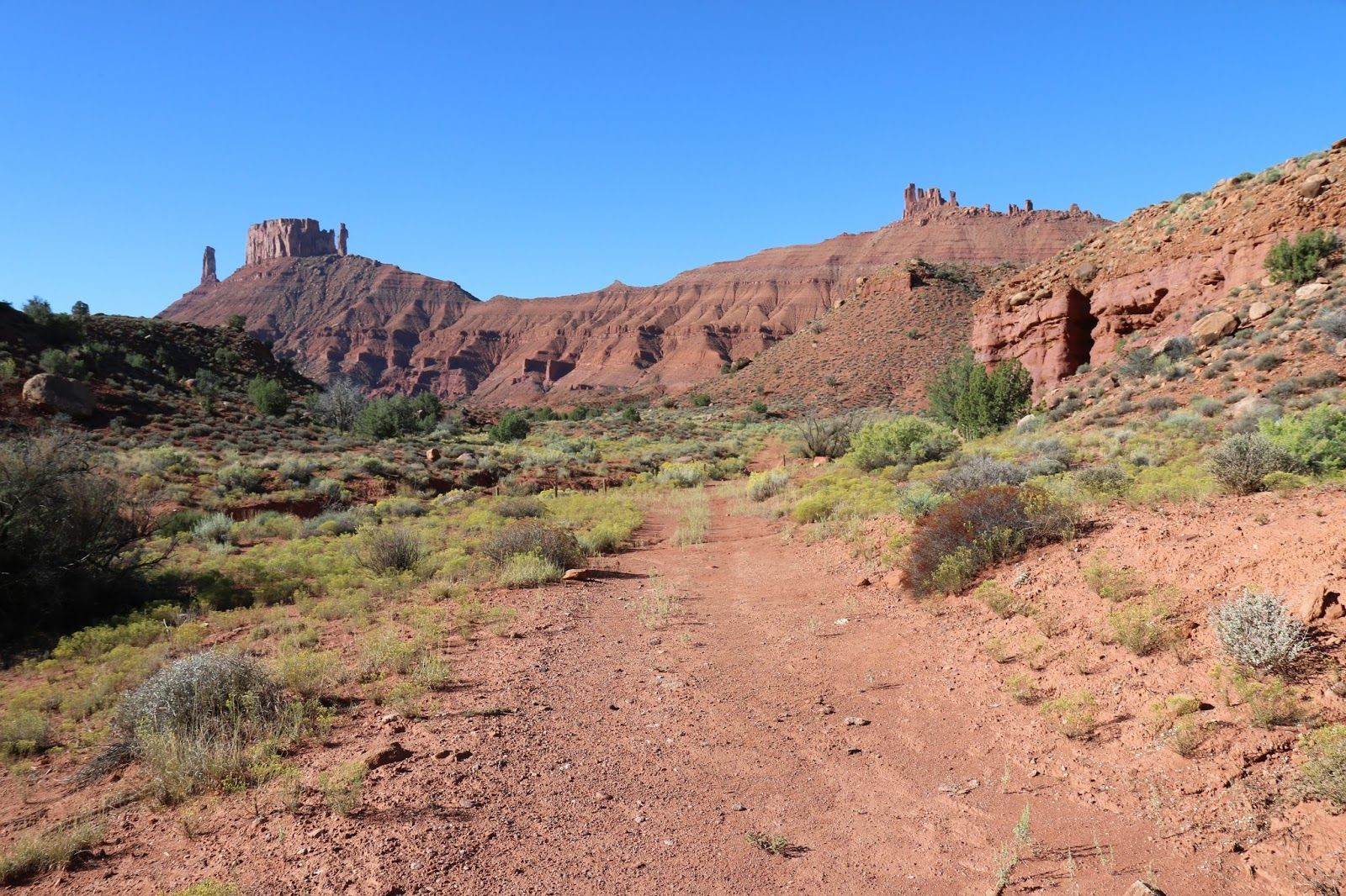 Desert trail leading toward red sandstone cliffs under a clear blue sky