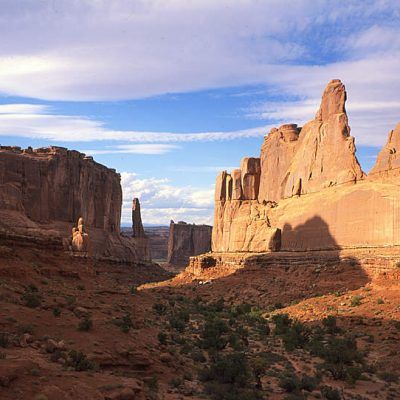Sunlit red rock canyon with towering desert cliffs under a partly cloudy blue sky