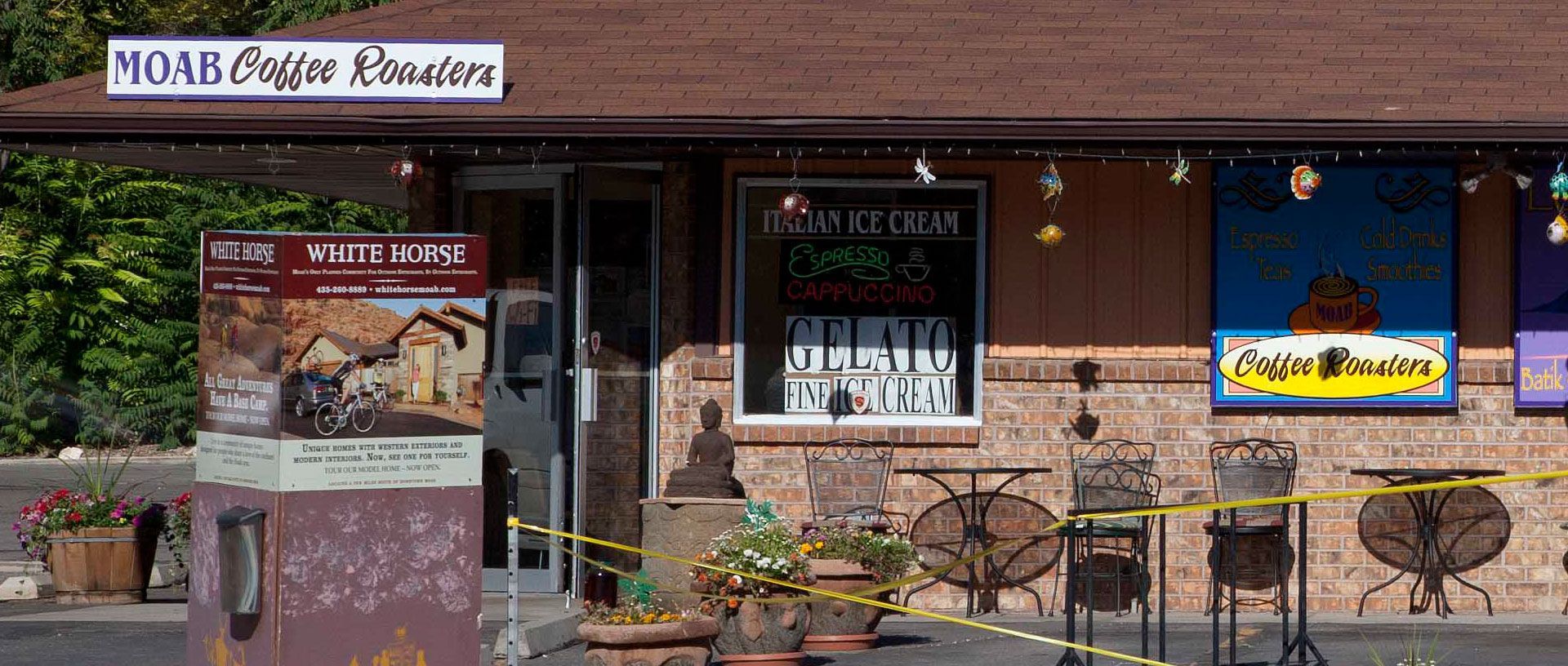 Storefront with sign reading “MOAB Coffee Roasters,” outdoor seating, and menu boards on a sunny street.
