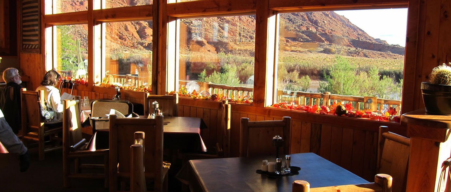 Cozy restaurant with wooden tables and chairs, large windows, and a canyon view in warm sunlight
