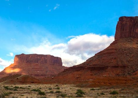 Red rock mesas under a bright blue sky with white clouds in a desert landscape