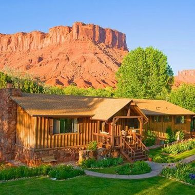 Rustic cabin in a green garden with red sandstone cliffs and blue sky in the background