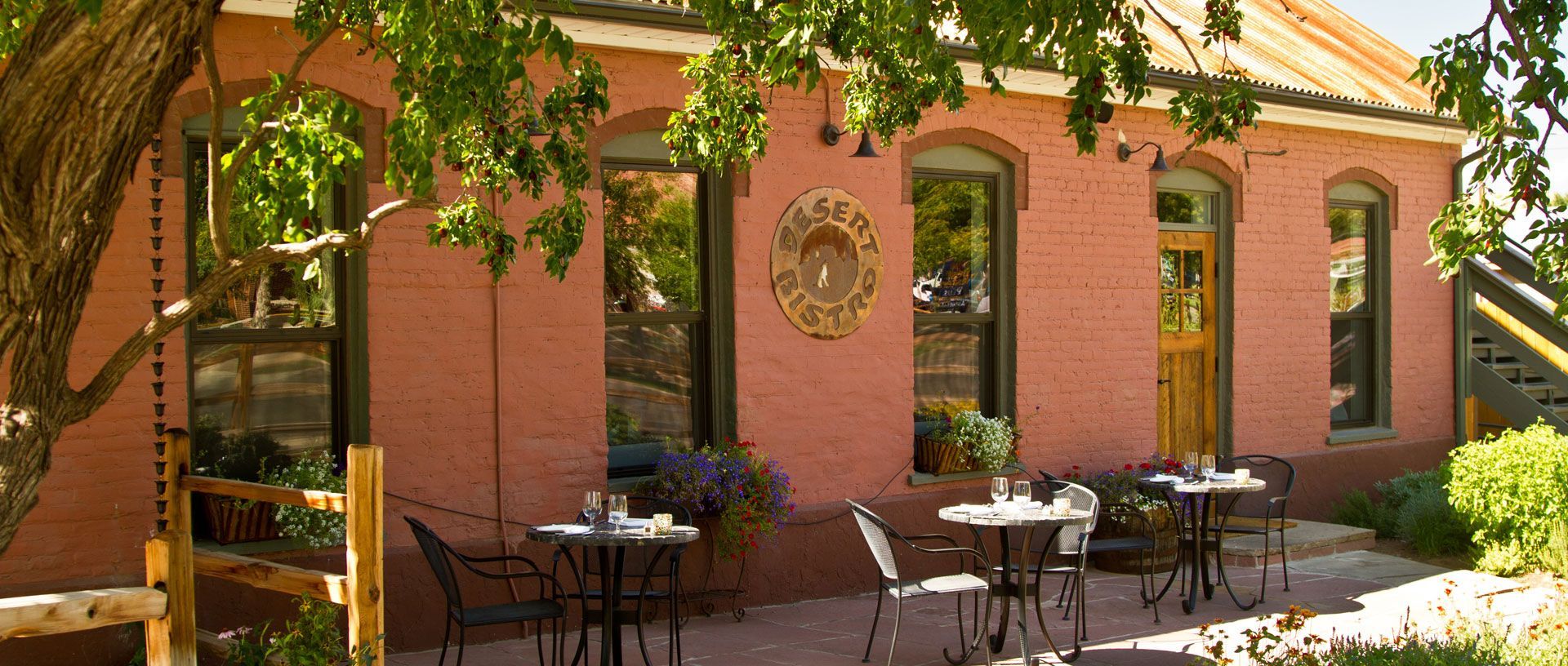 Courtyard with brick building, arched windows, patio tables and chairs under a leafy tree