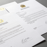 Dos documentos firmados con aspecto oficial y sello dorado, apilados sobre una superficie blanca.