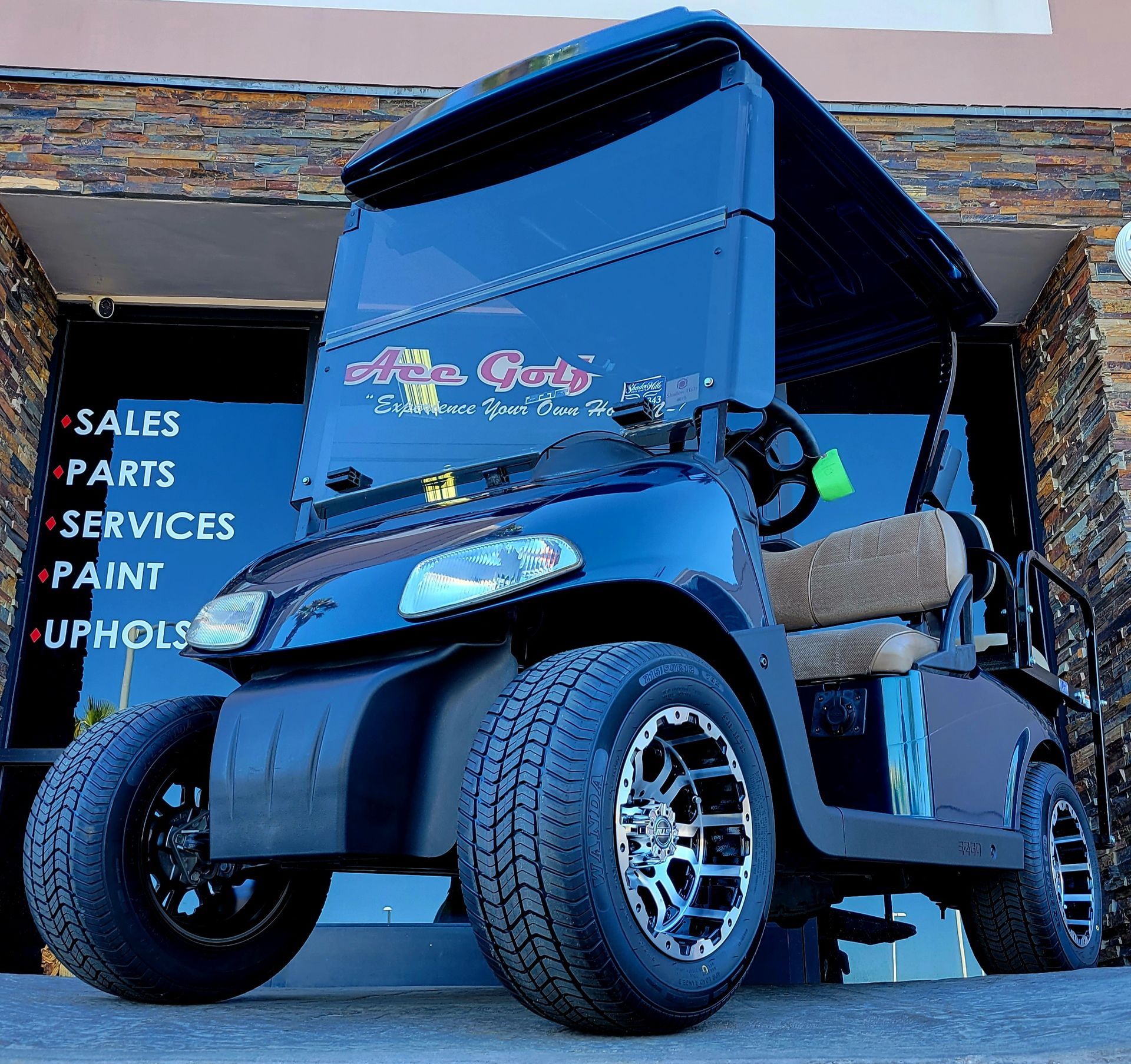 A black golf cart is parked in front of a building that says sales parts services paint uphols