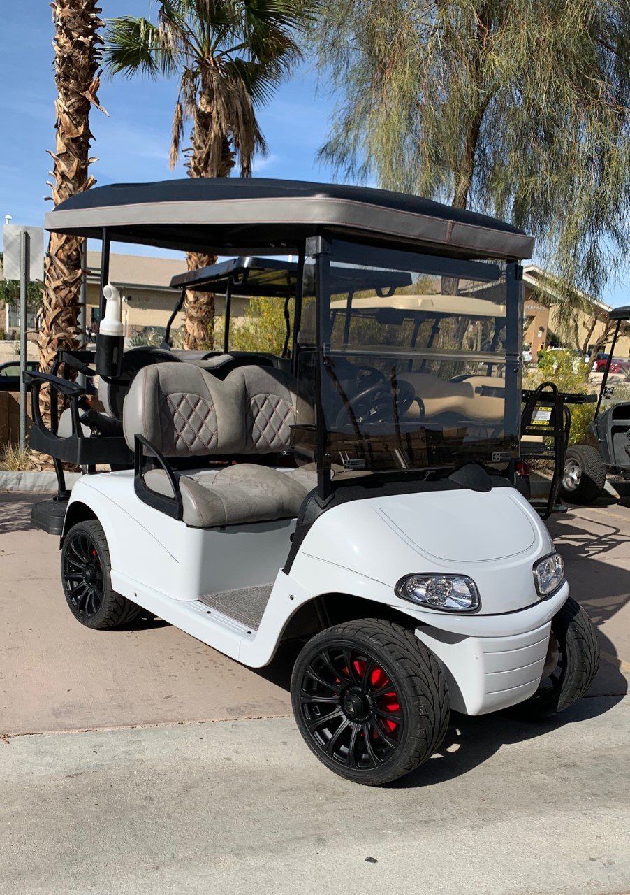 A white golf cart is parked on the side of the road next to a palm tree.
