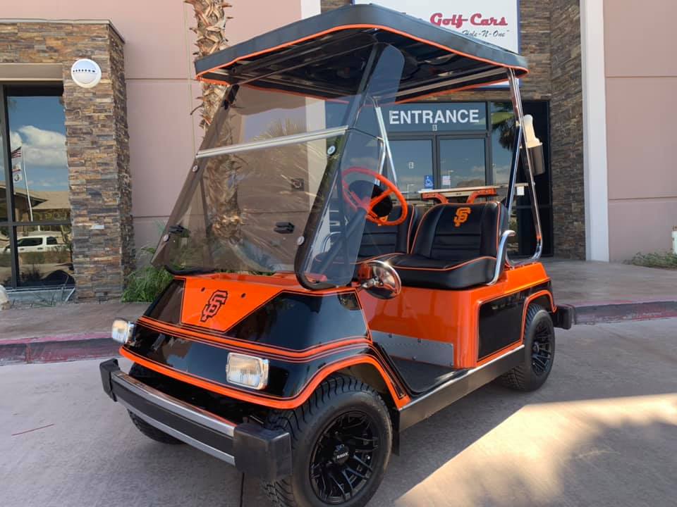 A black and orange golf cart is parked in front of a building that says entrance