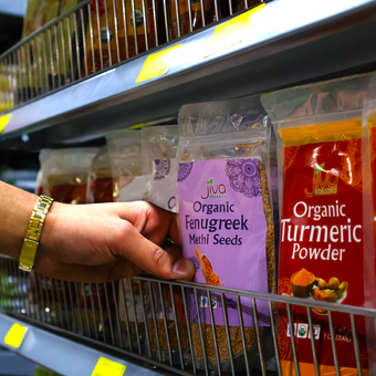 A person is reaching for a bag of organic fenugreek seeds