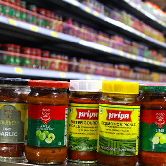 Several jars of priya pickles are lined up on a shelf